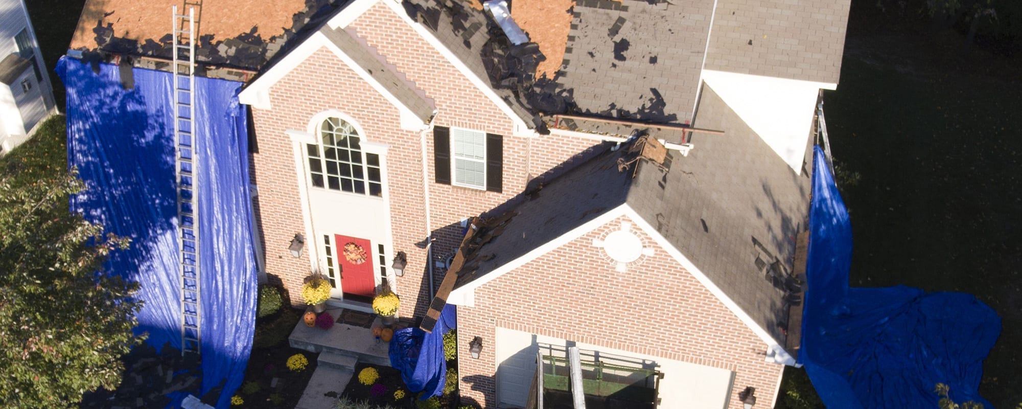 Aerial view of a home with tarps covering exposed roof decking after storm damage